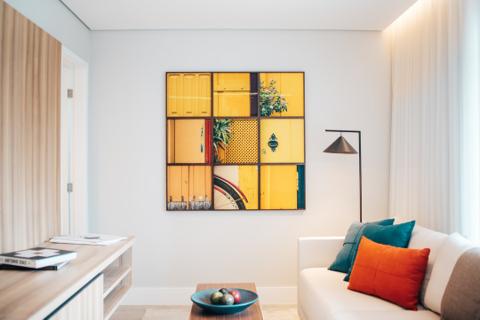 A vibrant wall art piece above the chairs, showing a cultural parade with people dressed in orange and yellow under a bright blue sky.